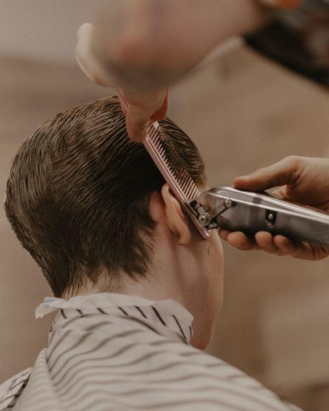 Un peluquero repasa con máquina y peine el corte de un cliente.